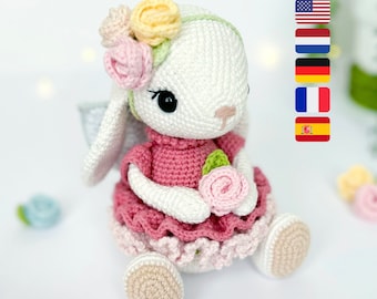 Puede incluir: Un conejito de crochet con un vestido rosa y una corona de flores. El conejito está sosteniendo una flor rosa en sus patas.
