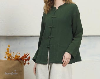 Può includere: Una donna indossa una giacca verde scuro con tre bottoni e pantaloni a gamba larga beige chiaro. La giacca ha maniche lunghe e un colletto alla coreana. I pantaloni sono di colore neutro. L'outfit è casual e confortevole.