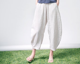 Puede incluir: Una mujer con una camisa azul marino de manga corta con un bolsillo y pantalones de lino blancos. Está de pie sobre una superficie verde.