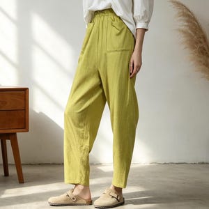Puede incluir: Una persona con una blusa blanca con cuello en V y pantalones verde claro con bolsillos. Los pantalones se combinan con zapatos beige sin cordones. El atuendo es informal y cómodo, adecuado para el uso diario.