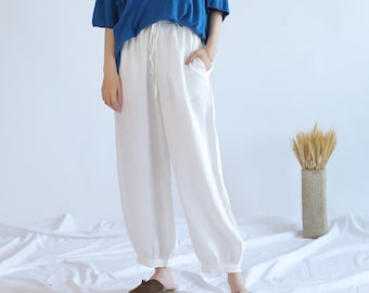 May include: White linen trousers with a drawstring waist and a relaxed fit. The trousers are shown on a model wearing a blue shirt.