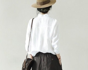 May include: A woman wearing a white button-down shirt, a brown fedora, a brown skirt, and black shoes. She is carrying a brown leather bag.