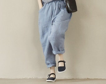 May include: A person wearing a straw hat, holding a book, and dressed in a blue and white plaid collared shirt, light blue trousers, and black shoes. A small black bag hangs from the shoulder.