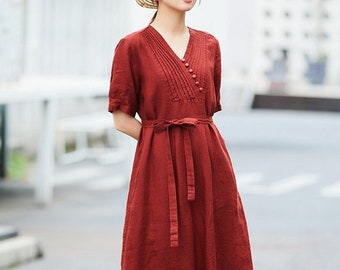 Pode incluir: Um vestido de linho vermelho com decote em V, mangas curtas e cinto de laço. O vestido tem um detalhe plissado na frente e um fecho de botão.