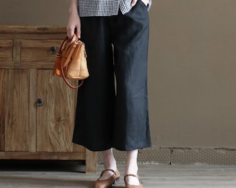 May include: A woman is wearing a black and white gingham button-up shirt with short sleeves and black wide-leg pants. She is holding a brown leather handbag.