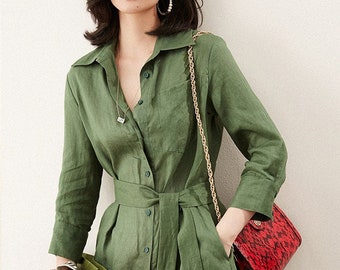May include: A green linen shirt dress with a button-up front, a tie belt, and a long sleeve. The dress has a pocket on the left side and is worn with a red snakeskin handbag.