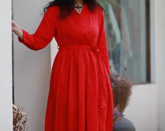 May include: A long red dress with a V-neckline and a tie belt. The dress is made of a lightweight fabric and has a flowy silhouette.