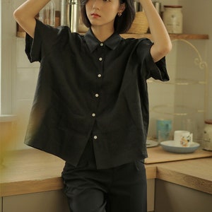 May include: A black collared shirt with short sleeves and a button-up front. The shirt is made of a lightweight fabric and has a relaxed fit.