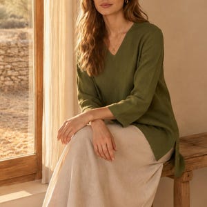 May include: An olive green V-neck tunic with three-quarter length sleeves and side slits, paired with a long, flowing cream-colored skirt. The tunic features a simple, straight-cut design that falls to the mid-thigh, while the skirt reaches the ankles.