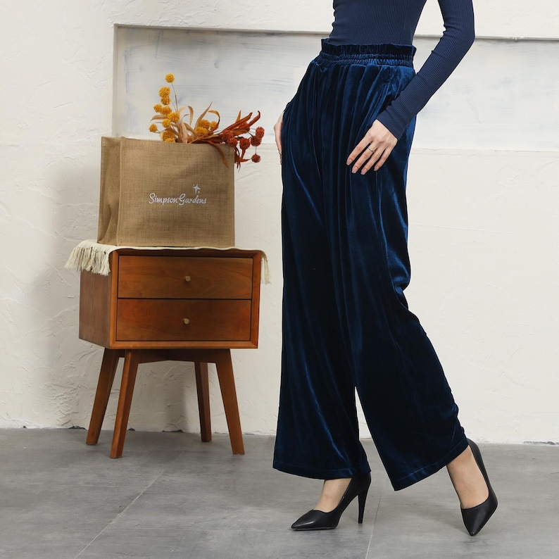 May include: A pair of wide-leg, dark blue velvet pants with a high waist and a slightly flared hem. The pants are made of a soft, luxurious fabric and have a relaxed fit.