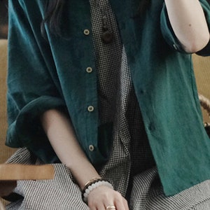 May include: A teal green linen shirt with a button-up front and long sleeves. The shirt is worn over a black and white checkered dress.