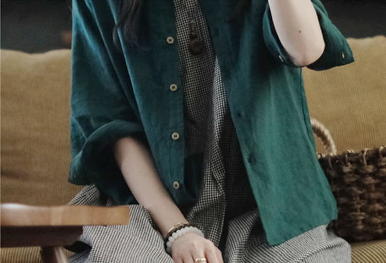 May include: A teal green linen shirt with a button-up front and long sleeves. The shirt is worn over a black and white checkered dress.