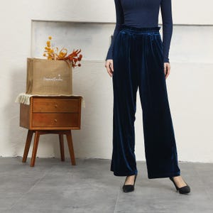 May include: A woman wearing a dark blue velvet wide-leg pant with a high waist and a dark blue top.