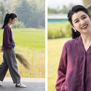 May include: A woman wearing a purple linen shirt with a v-neck and long sleeves. She is smiling and looking at the camera. The shirt has a button closure at the neck.