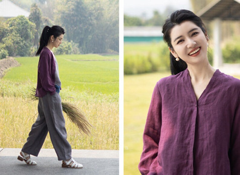 May include: A woman wearing a purple linen shirt with a v-neck and long sleeves. She is smiling and looking at the camera. The shirt has a button closure at the neck.