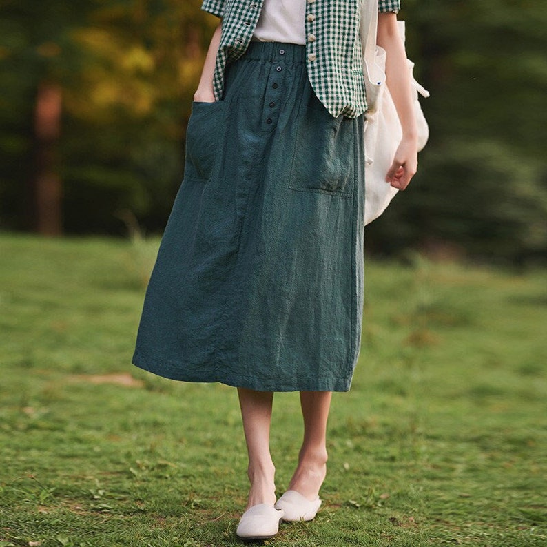 May include: A teal green midi skirt with a button closure and two large pockets. The skirt is made of a soft, linen-like fabric.
