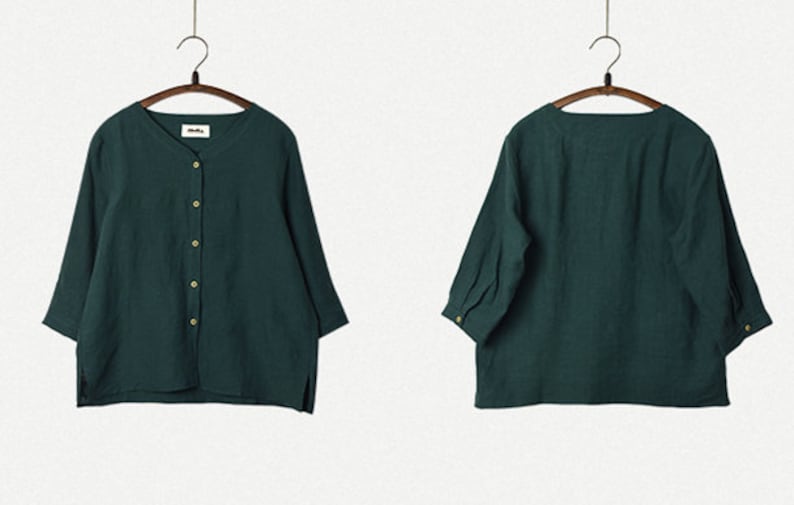 May include: A dark green, button-up shirt with three-quarter sleeves. The shirt is hanging on a wooden hanger.