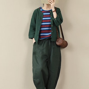 May include: A woman wearing a green cardigan over a striped shirt, green linen pants, and white sneakers. She is carrying a brown leather bag.