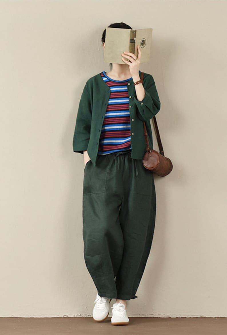 May include: A woman wearing a green cardigan over a striped shirt, green linen pants, and white sneakers. She is carrying a brown leather bag.