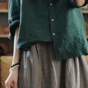May include: A green linen button-down shirt with long sleeves and a black and white gingham skirt.
