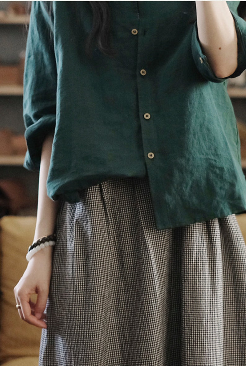 May include: A green linen button-down shirt with long sleeves and a black and white gingham skirt.