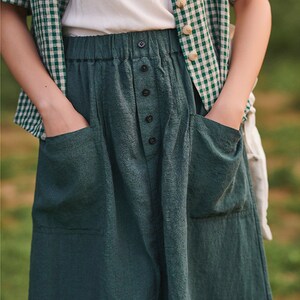 May include: A dark green linen skirt with a button fastening and two large pockets. The skirt has a high waist and a relaxed fit.