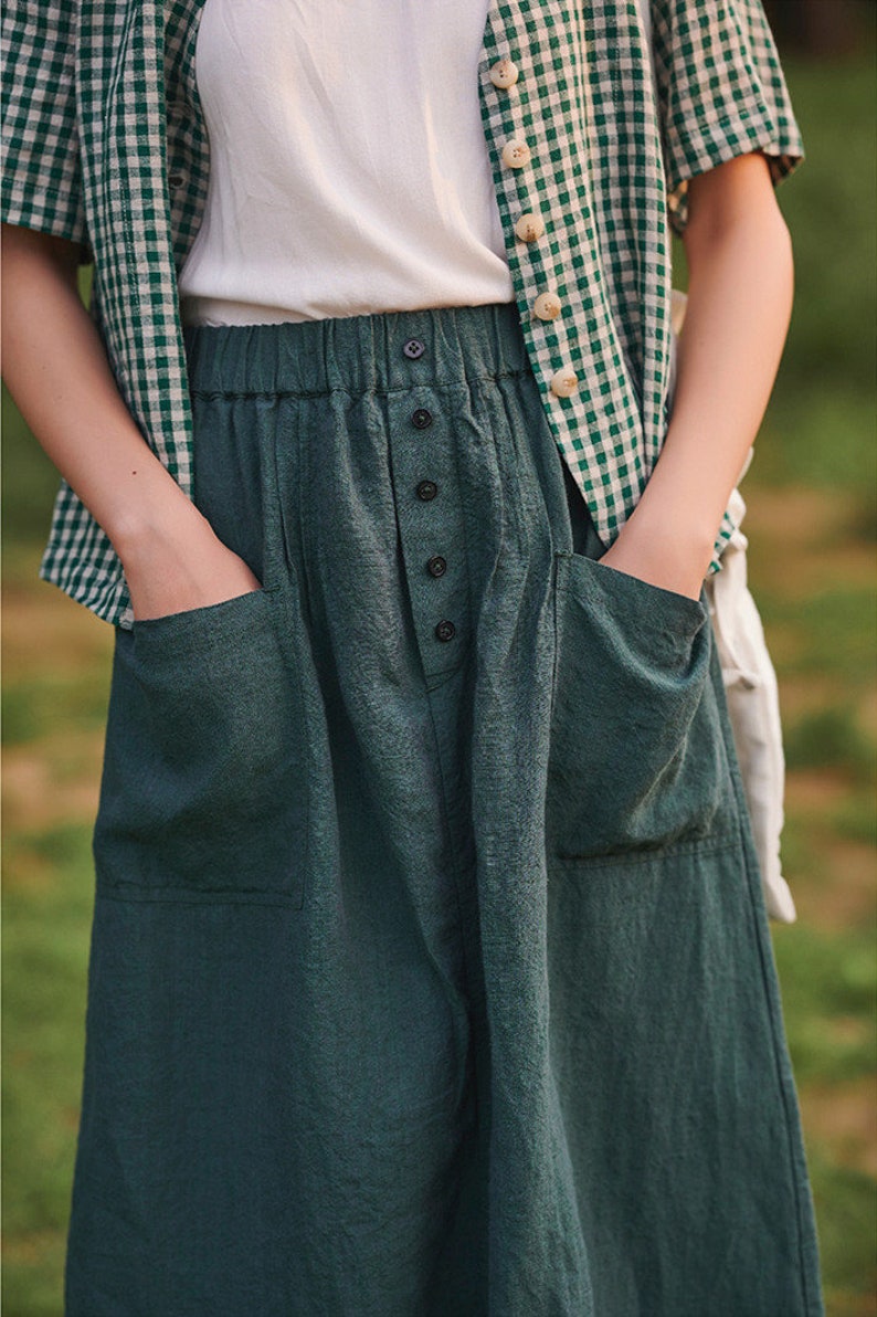 May include: A dark green linen skirt with a button fastening and two large pockets. The skirt has a high waist and a relaxed fit.