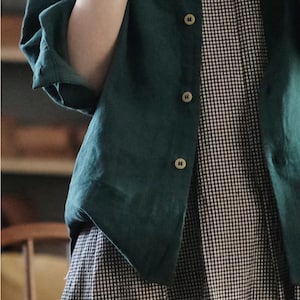 May include: A green linen shirt with a black and white gingham pattern underneath. The shirt has a button-up front and long sleeves.