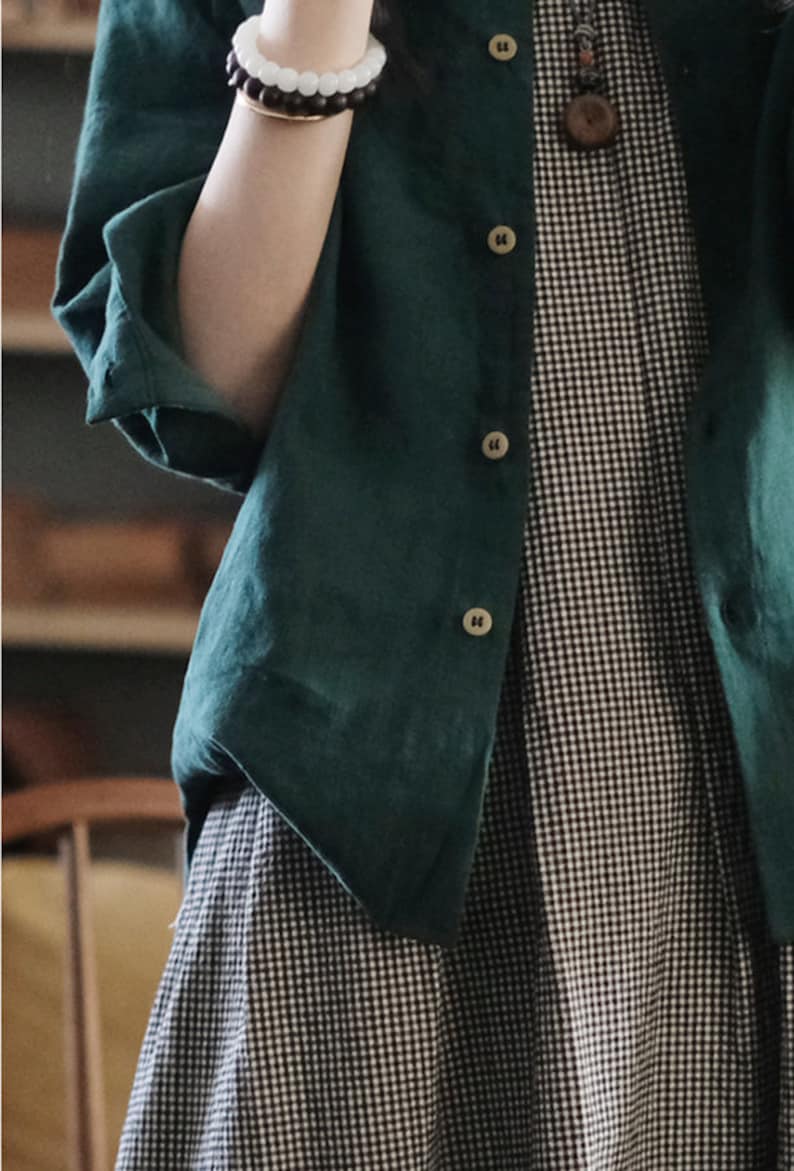 May include: A green linen shirt with a black and white gingham pattern underneath. The shirt has a button-up front and long sleeves.