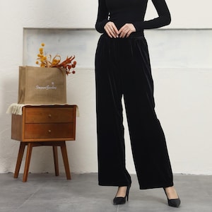 May include: Black velvet wide-leg pants with a high waist and a relaxed fit. The pants are shown on a model wearing a black turtleneck top and black heels.