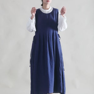 Puede incluir: Una mujer con un vestido de lino azul y una blusa blanca debajo. Lleva un sombrero de paja y zapatos marrones.