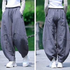 May include: Gray, loose-fitting pants with a unique, voluminous design. The pants feature large pockets and a comfortable, elastic waistband. The fabric appears to be a soft, breathable material, suitable for casual wear. The pants are paired with white sneakers.