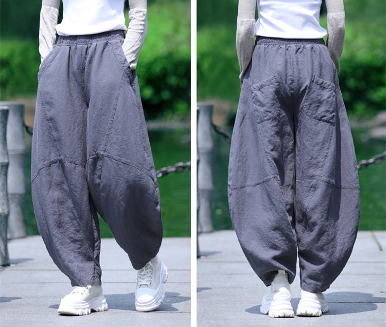 May include: Gray, loose-fitting pants with a unique, voluminous design. The pants feature large pockets and a comfortable, elastic waistband. The fabric appears to be a soft, breathable material, suitable for casual wear. The pants are paired with white sneakers.