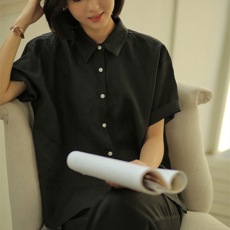 May include: A black short-sleeved button-down shirt with a relaxed fit. The shirt is made of a lightweight fabric and has a collar.