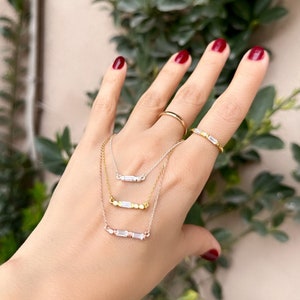 May include: Three gold necklaces with different lengths and styles. Each necklace features a bar pendant with clear cubic zirconia stones.