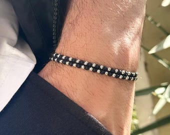 May include: A black and silver beaded bracelet with a double row of beads. The bracelet is worn on a person's wrist.