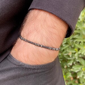 May include: A black beaded bracelet with silver accents. The bracelet is worn on a person's wrist.