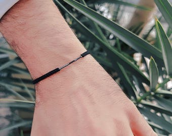 Può includere: Un braccialetto in corda nero con un accento a barra argentata.