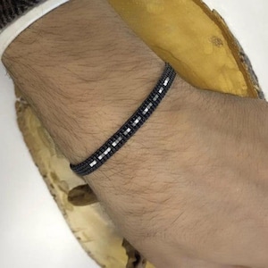 May include: A black and white beaded bracelet on a person's wrist. The bracelet is made of small, square beads.