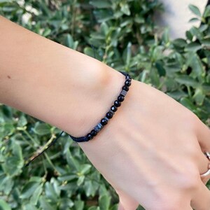 Könnte beinhalten: Ein schwarzes Armband mit schwarzen und silbernen Perlen auf einem schwarzen Band.