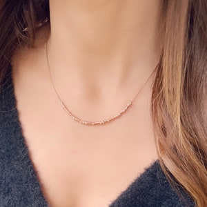 May include: A delicate rose gold necklace featuring a series of small, evenly spaced beads and textured accents. The necklace is displayed against a soft background, highlighting its minimalist design and elegant simplicity. This piece is a subtle yet stylish accessory.