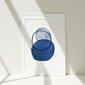 Puede incluir: Una impresión enmarcada con un diseño abstracto minimalista que presenta dos círculos azules de acuarela superpuestos. El círculo más grande es de un azul más oscuro y el círculo más pequeño es de un azul más claro.