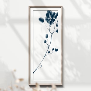 Può includere: Una stampa incorniciata di un dipinto ad acquerello blu di un ramo delicato con piccoli fiori blu. Il dipinto è su sfondo bianco ed è incorniciato in una cornice di legno chiaro.