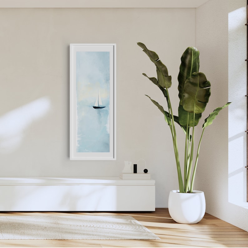 Peut inclure: Une impression encadr&eacute;e blanche d'une peinture &agrave; l'aquarelle repr&eacute;sentant un voilier sur une &eacute;tendue d'eau calme. La peinture est accroch&eacute;e &agrave; un mur blanc au-dessus d'un banc blanc. Une grande plante verte dans un pot blanc se trouve dans le coin de la pi&egrave;ce.