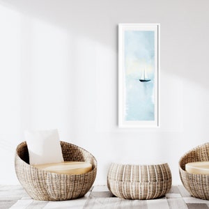 Peut inclure: Deux chaises en osier avec coussins et un pouf en osier devant un mur blanc avec une peinture aquarelle encadr&eacute;e d'un voilier sur l'eau.