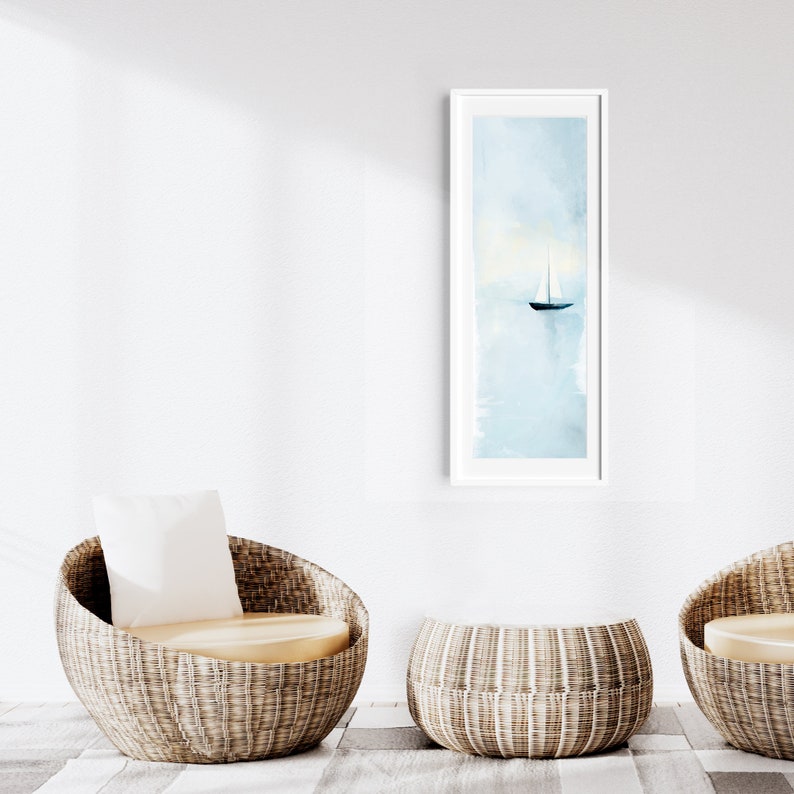 Peut inclure: Deux chaises en osier avec coussins et un pouf en osier devant un mur blanc avec une peinture aquarelle encadr&eacute;e d'un voilier sur l'eau.