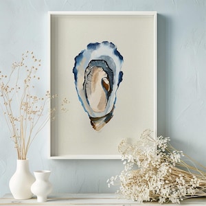 May include: Watercolor painting of an oyster shell in a white frame. The shell is depicted with shades of blue, brown, and beige against a light background. The artwork is displayed on a light blue wall, with white vases and dried flowers in the foreground.