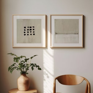 May include: Two framed abstract art prints with a light beige background. The print on the left has a black grid pattern. The print on the right has a horizontal line dividing the background into two shades of beige.