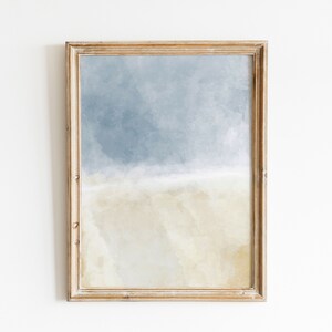 May include: A framed abstract painting with a light blue and beige color scheme. The painting depicts a sky with clouds and a sandy beach.