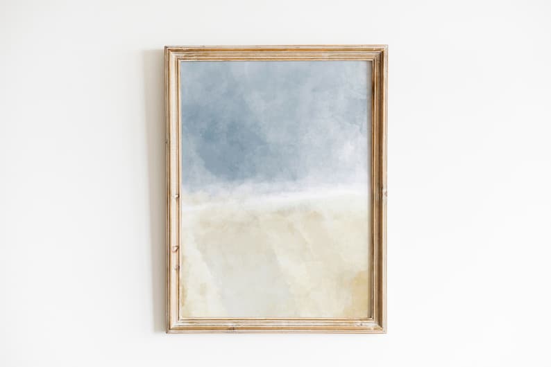 May include: A framed abstract painting with a light blue and beige color scheme. The painting depicts a sky with clouds and a sandy beach.
